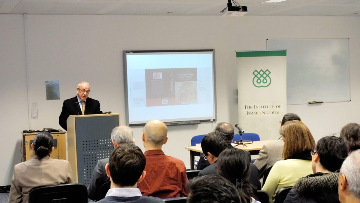 A person addressing the audience with a presentation on a projector in the back ground
