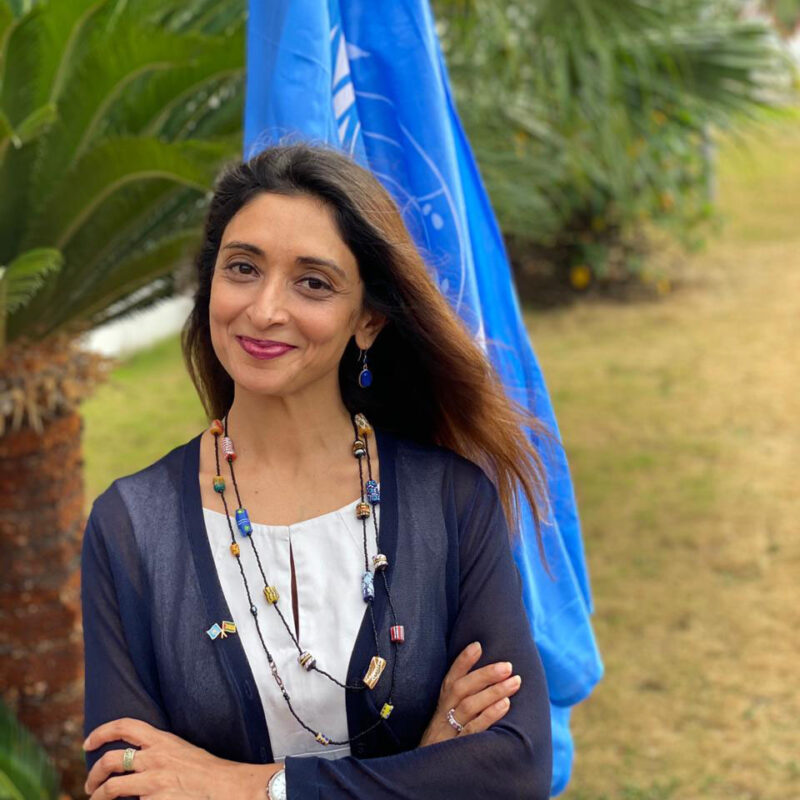 An IIS alumna Zahra Virani wearing a blue-white shirt and posing for a picture