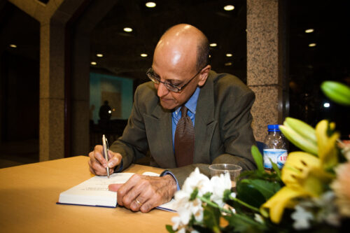 A man in grey suit sitting and signing a book