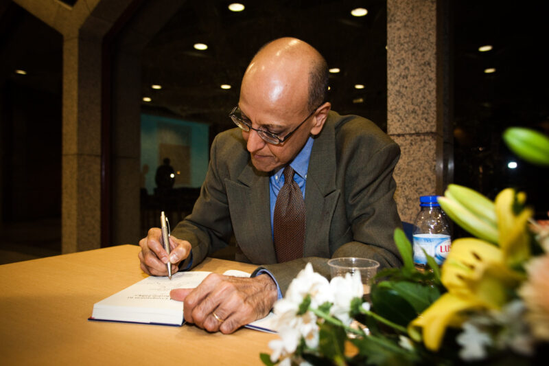 A man in grey suit sitting and signing a book