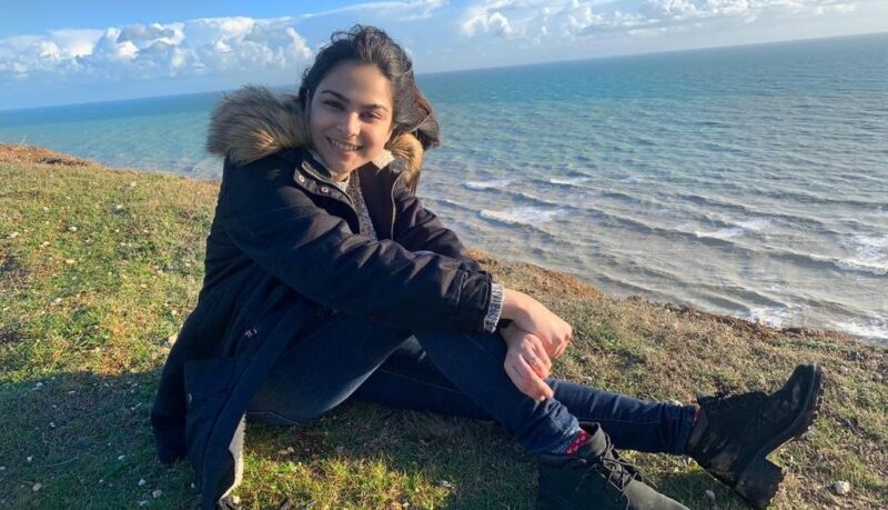 STEP student sitting in a garden wearing a winter jacket with her legs stretched in a sea view