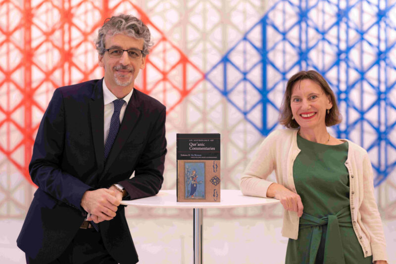 Dr Karen Bauer and Dr Feras Hamza leaning from the side with their opposite arms on the table with a printed copy of their book in the centre and posing