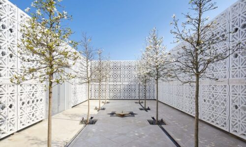 An image of AKC terrace with six trees on the side and a fountain in the centre surrounded with white geometrical designed walls