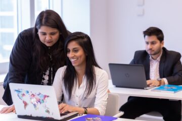 Two STEP students working together in a laptop, (one sitting while the other standing on her left) and the third STEP student working independently