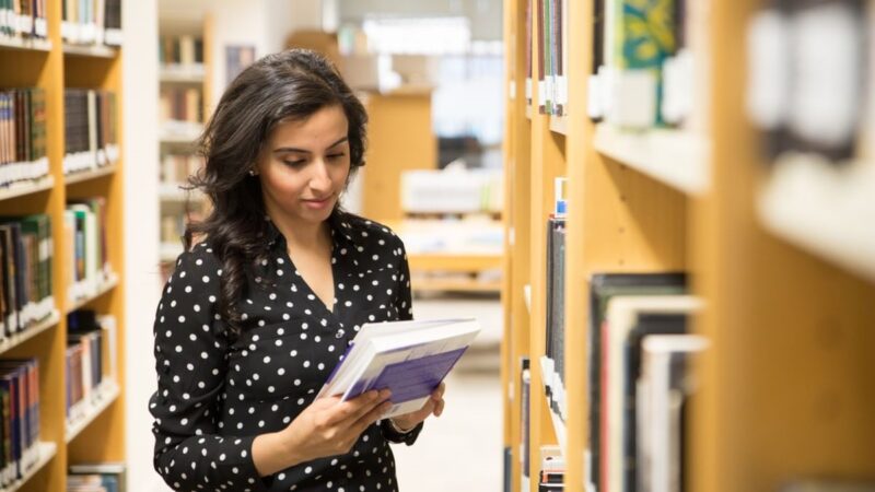 A STEP student in polka dot black dress standing in the corner of old IIS library (ground floor) and going through a book