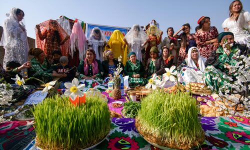 Tajiki Ismailis celebrating and posing for a picture in local dresses during their cultural festival in a group with food items in the front