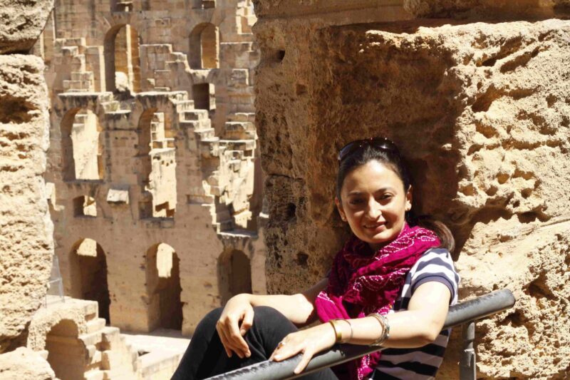 IIS employee Qudsia Shah sitting in an ancient architectural site holding a wall and posing for a picture