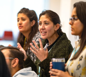 A side view of a student showing doing hand gestures and explaining something to the audience with one student each on left and right
