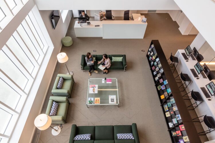 A view of the AKC library from the top of AKC, with people sitting on the reception and sofas utilising the library space