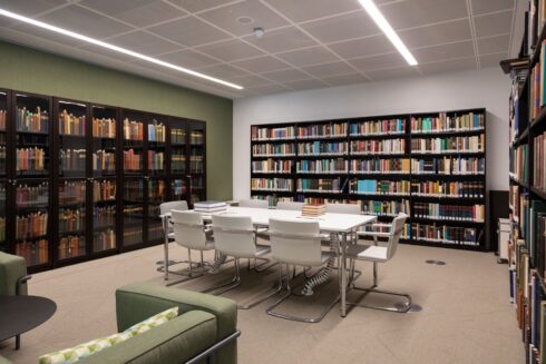 A view of a discussion room of Aga Khan Centre library from inside with book shelves on all three sides tables and chairs in a discussion set up, and some sofa chairs on the side with a small table in the centre