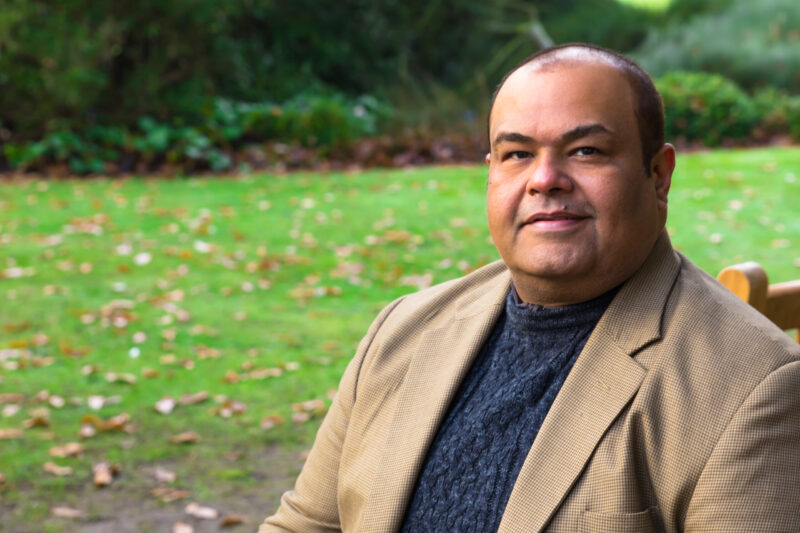 A man in light brown suit in a green outdoor background