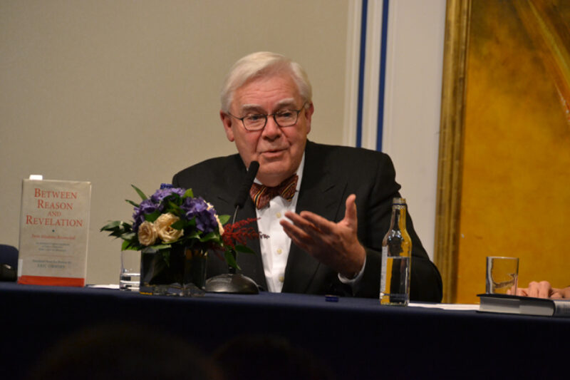 A man in black suit, white shirt speaking at a podium