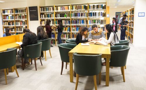 An overarching view from inside the IIS library with two students searching for books, three standing and reading, three sitting and studying their work while three others using one book to understand the content