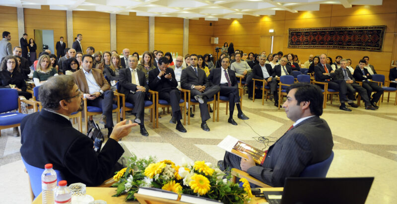 A group of people sitting in a semi circle and listening to two intellectuals talking to them