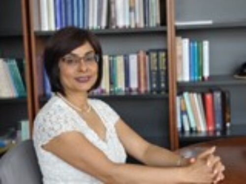 A lady in white shirt posing for a photo with some books stacked in the backshelf