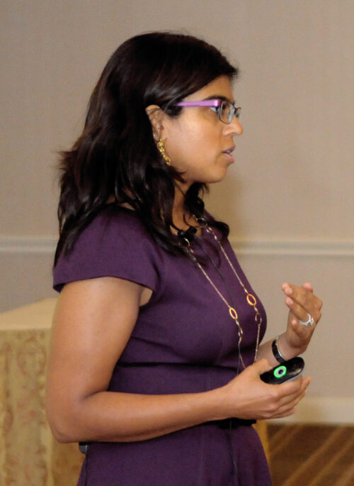 A left profile of woman in purple dress speaking about something